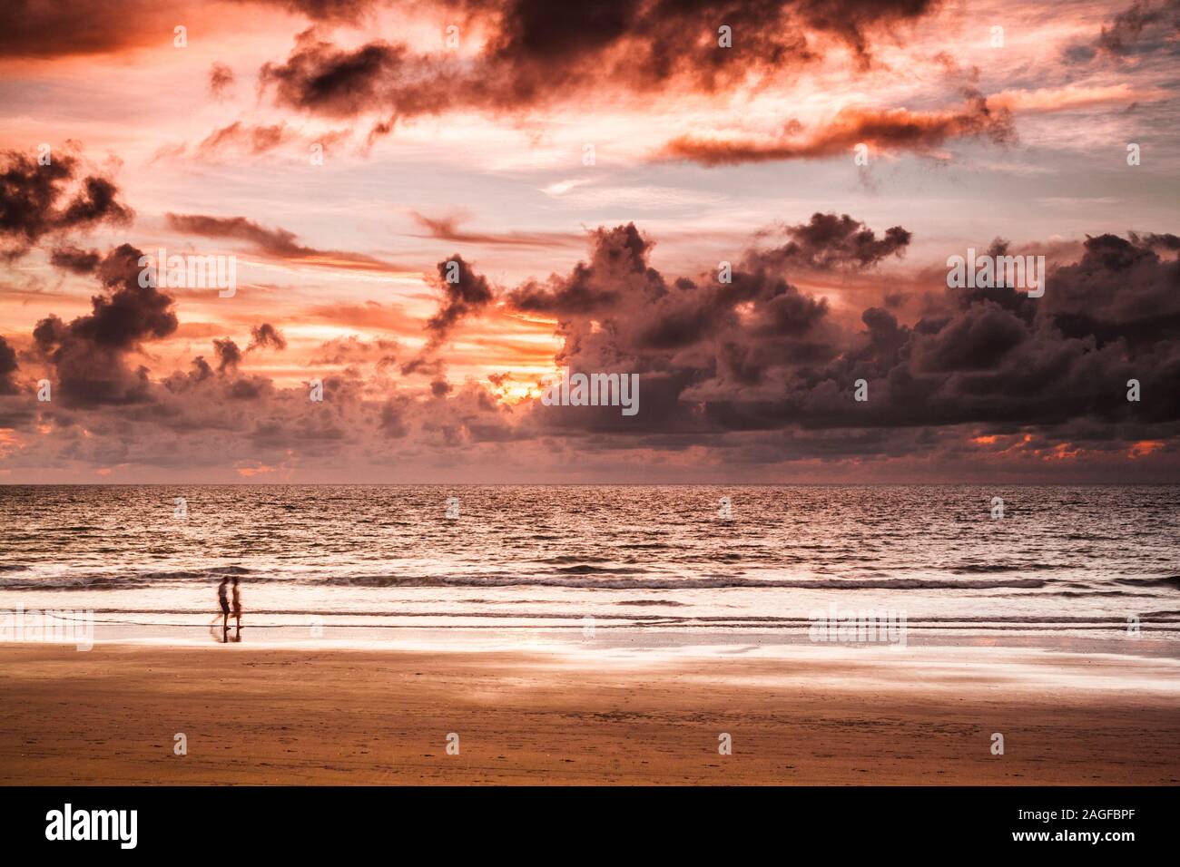 Due persone che passeggiano lungo la spiaggia con un drammatico tramonto Atlantico prese a Kololi in Gambia. Foto Stock