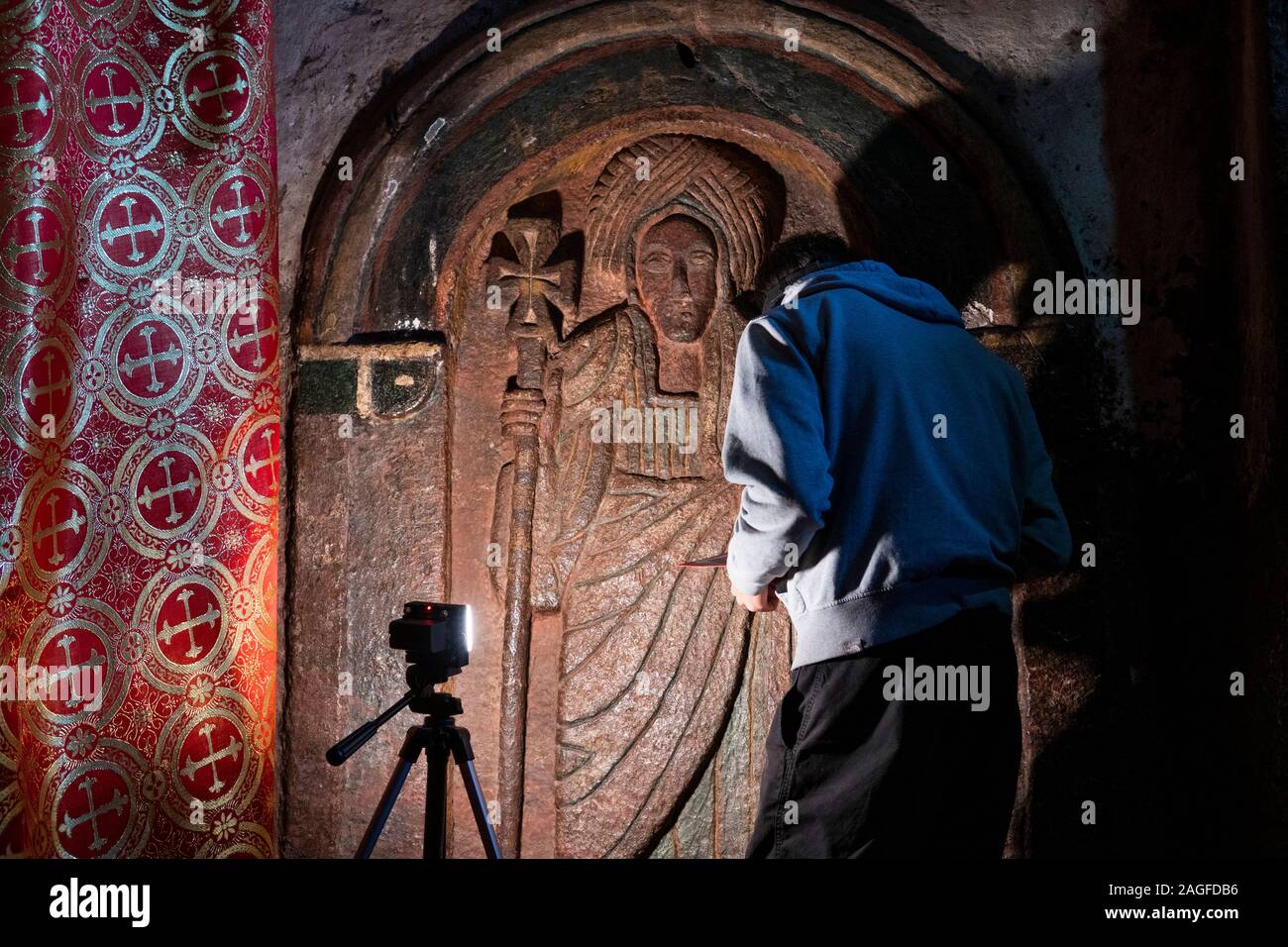 Eth1041 Etiopia, Amhara Region, Lalibela, Bet Golgota, sanctum, conservatore esaminando scolpita in pietra di dimensioni di vita apostolo figura con spia luminosa Foto Stock