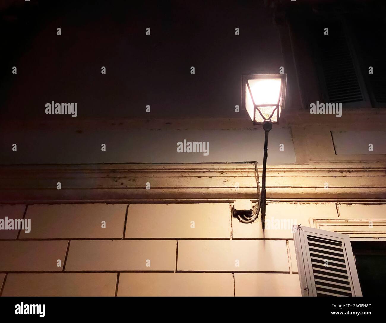 Antiche decorate in ferro battuto lampada di strada attaccata alla parete di un antico palazzo nel centro storico di Roma di notte. Il bagliore della luce sulla parete Foto Stock