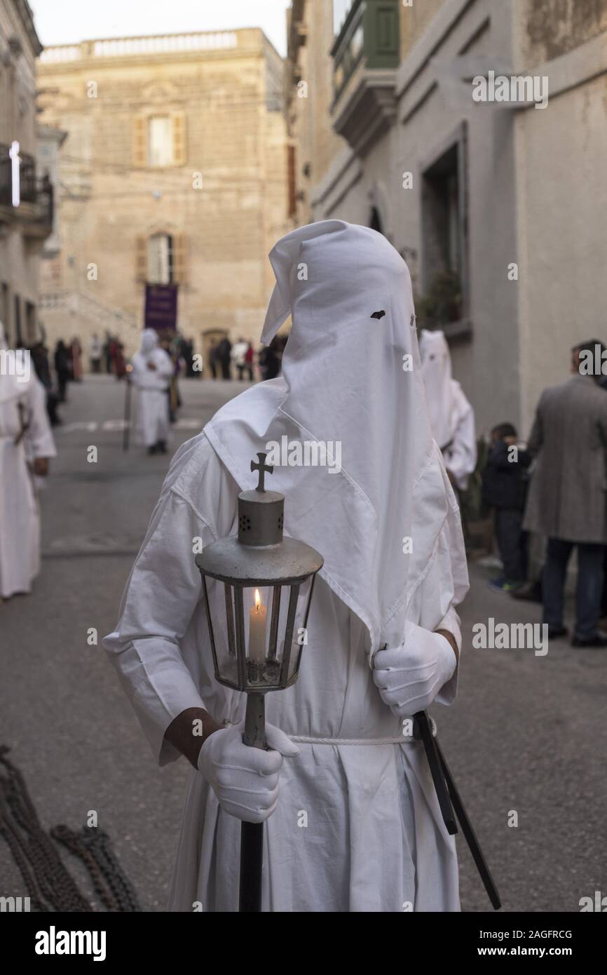 BAXXAR, Malta - 03 Apr 2015: Candida incappucciati penitente, portante una lanterna accesa e tenendo una croce in corda-cinghia, gli spettatori a guardare. Buona Frida Foto Stock