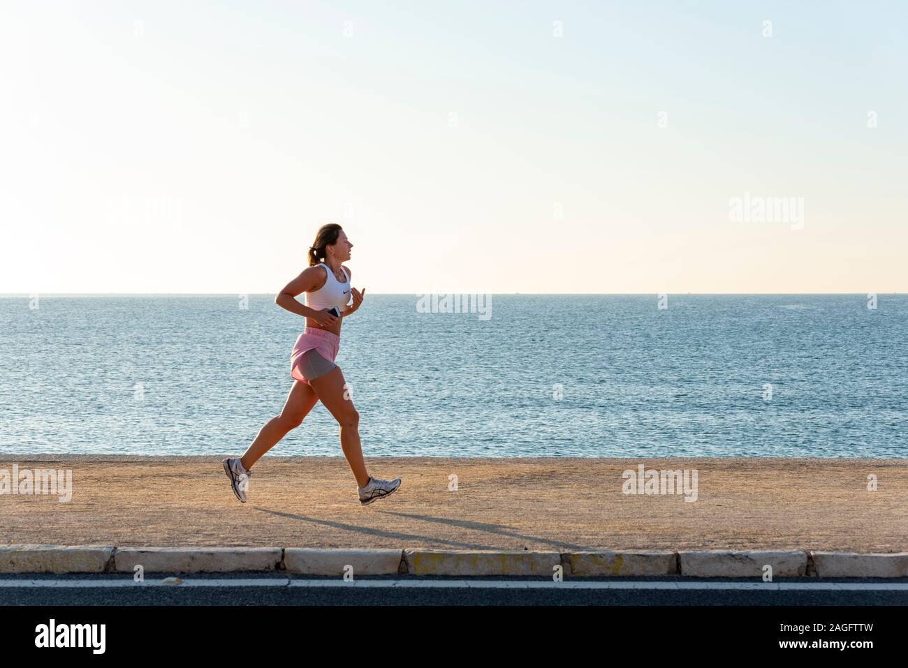 Donna jogging in spiaggia con un telefono, Alicante, Spagna Foto Stock