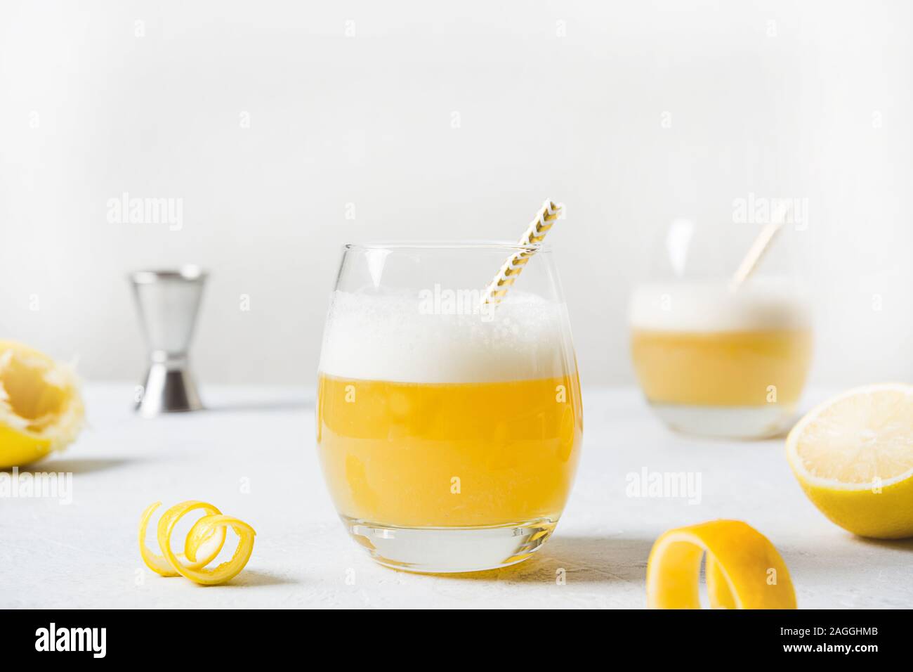 Il whiskey sour cocktail con gli ingredienti, il succo di limone e lo sciroppo di zucchero e albume in vetro sul tavolo bianco. Orientamento orizzontale. In casa bevanda. Foto Stock