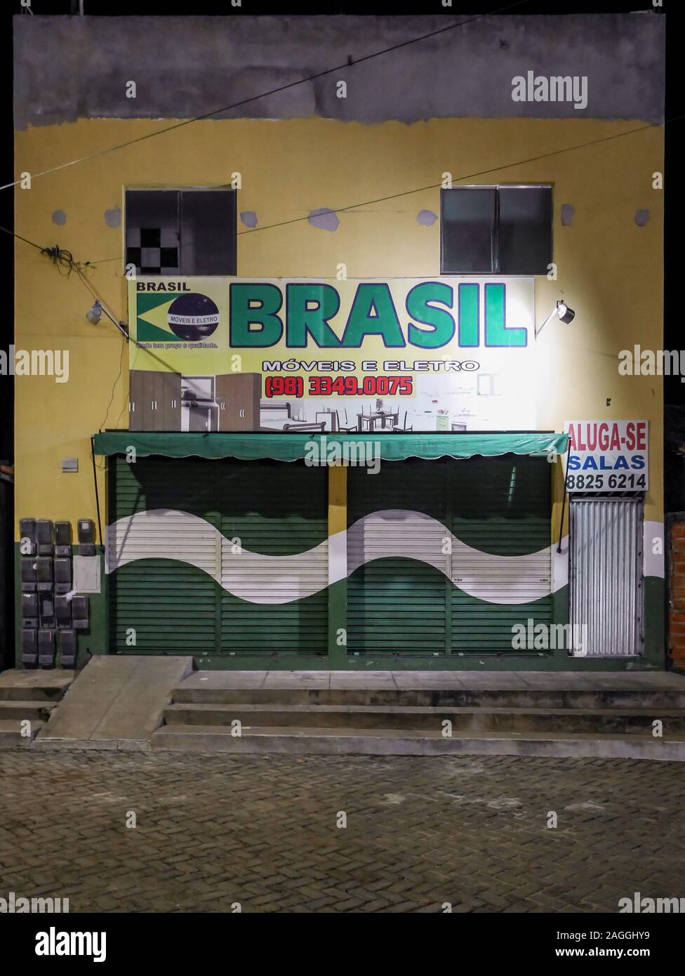 Un negozio chiuso davanti dipinte in colori nazionali di Brasile a tarda notte per le strade di Barrieirinhas nel nord del Brasile. Foto Stock