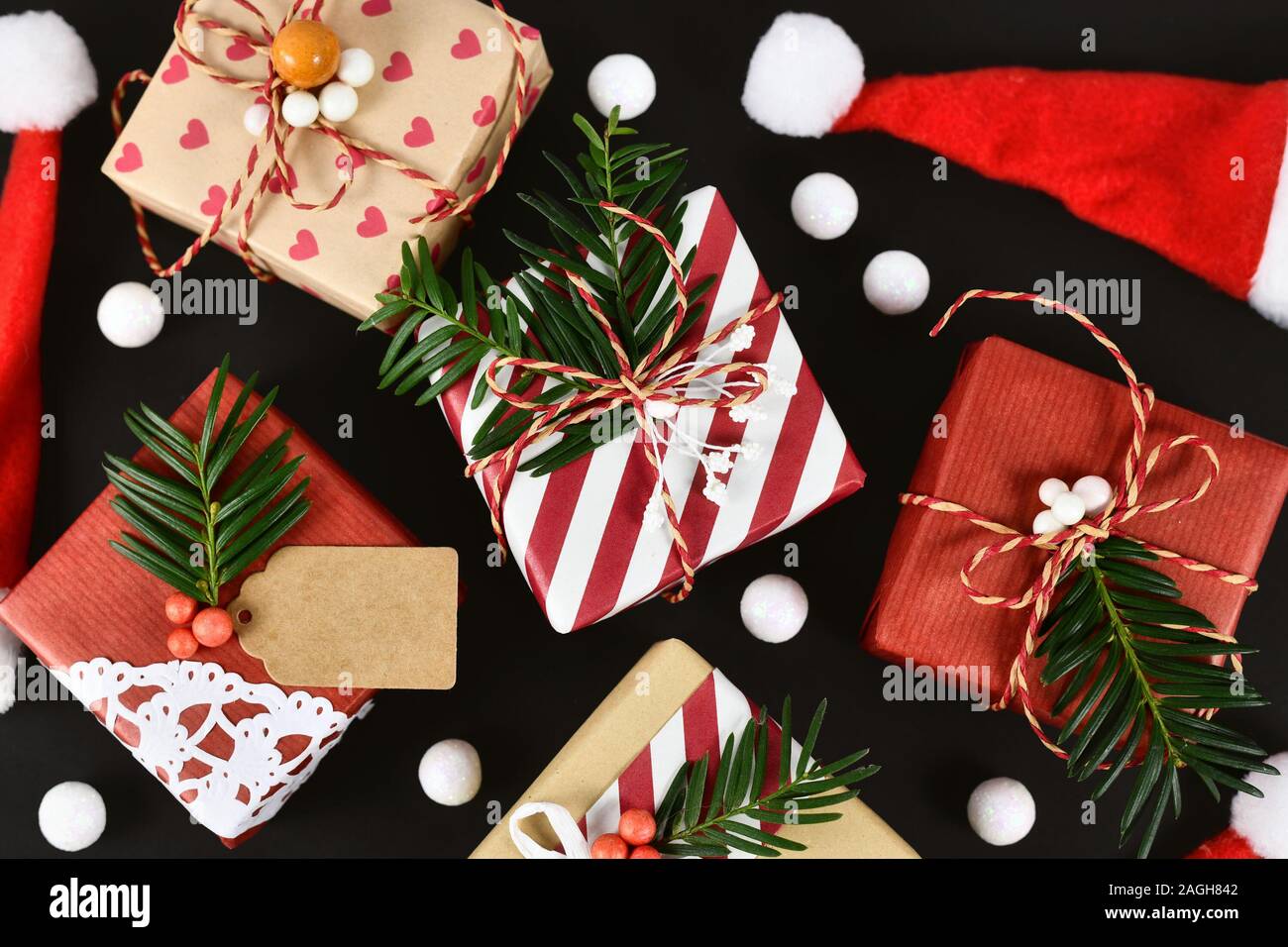 Vista superiore del bel rosso, bianco e marrone naturale decorato di Natale confezioni regalo con nastri e rami di abeti scuri su sfondo nero Foto Stock