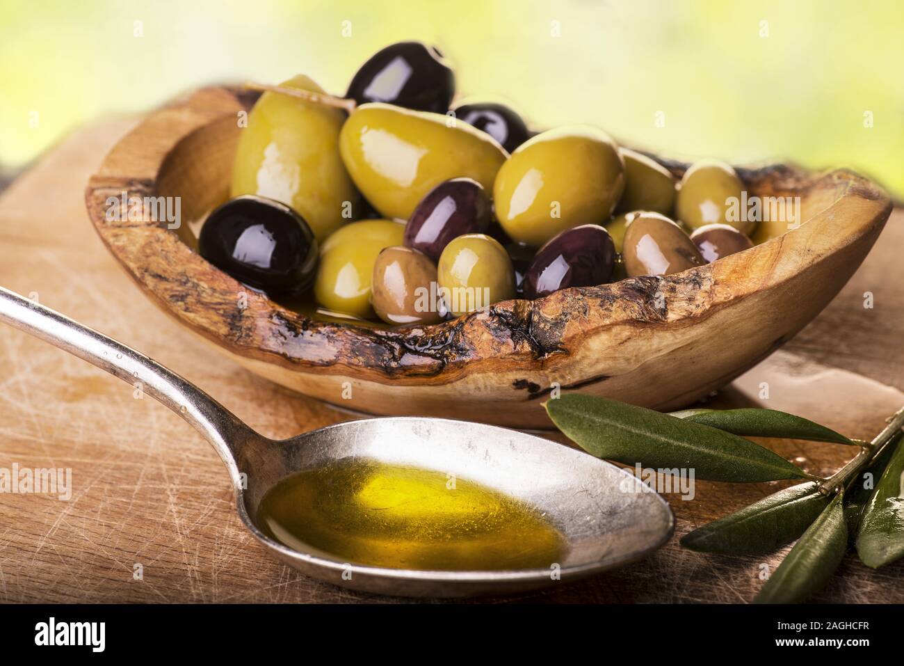 Sulla tavola in legno rustico, una ciotola con vari tipi di olive e un cucchiaio pieno di olio Foto Stock