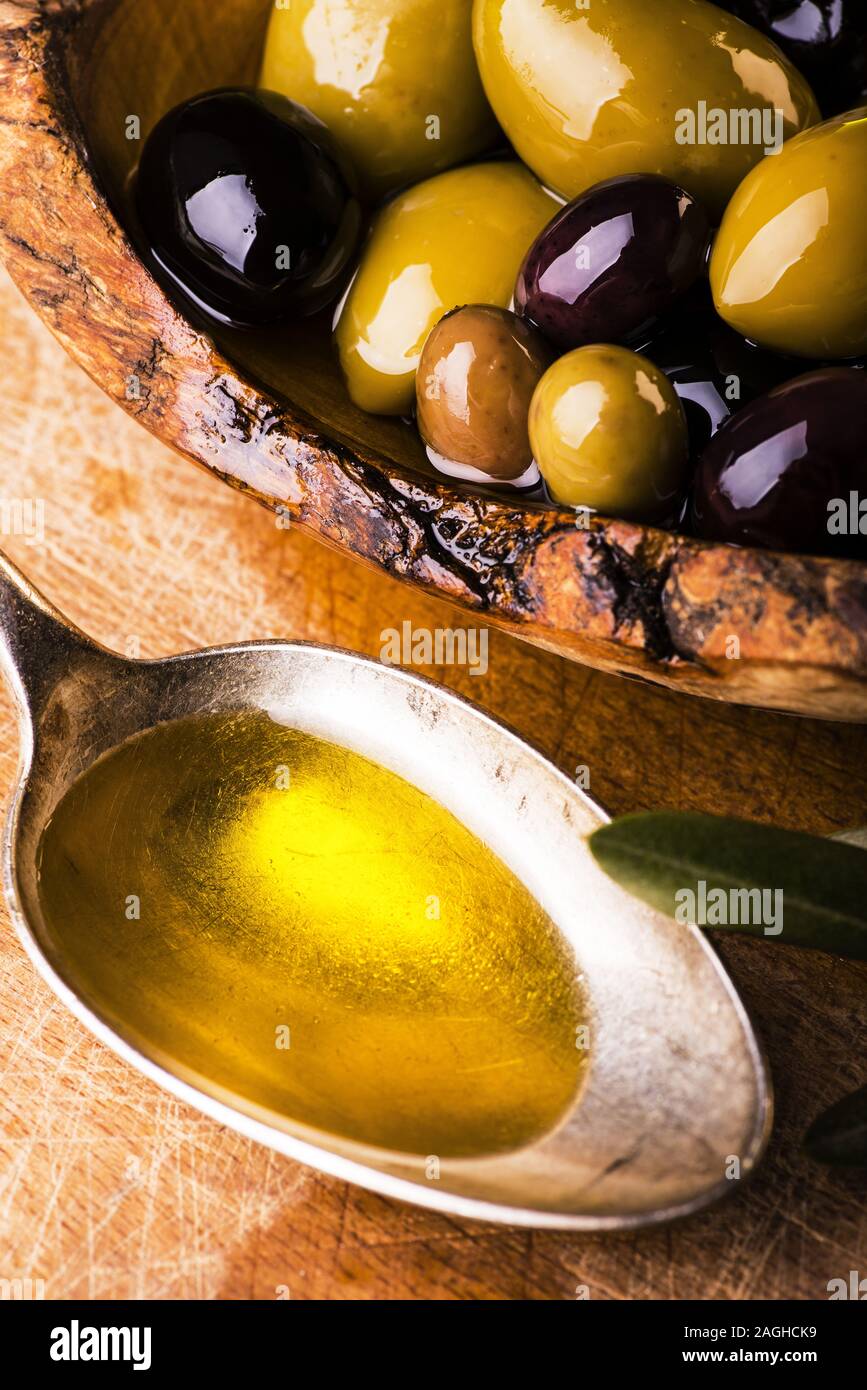 Sulla tavola in legno rustico, una ciotola con vari tipi di olive e un cucchiaio pieno di olio Foto Stock