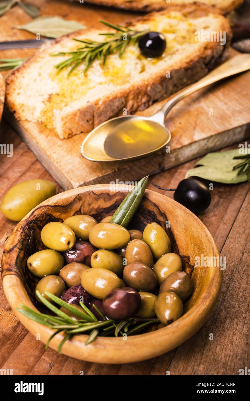 Sulla tavola in legno rustico, un cucchiaio pieno di olio delle olive e fette di pane Foto Stock