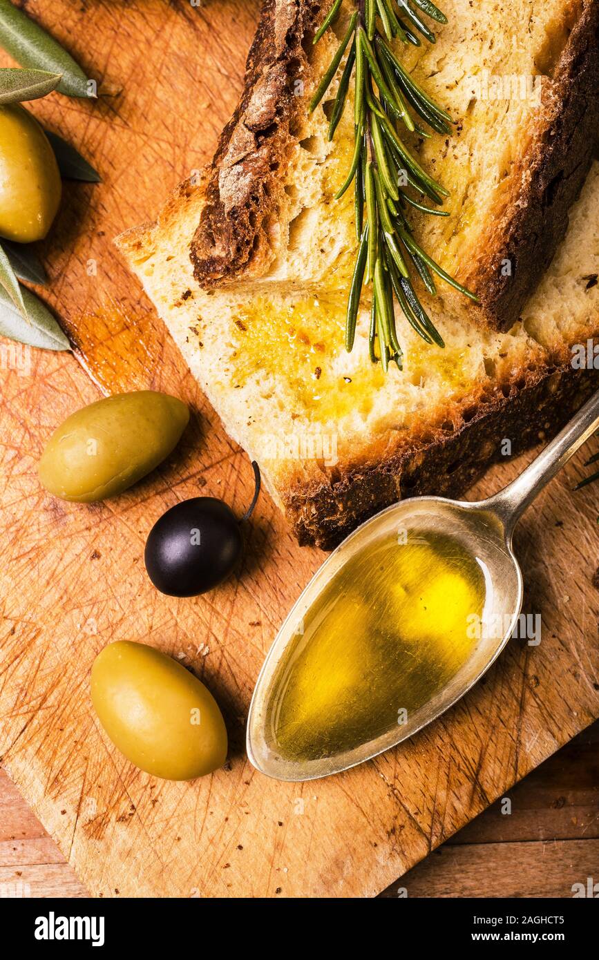 Sulla tavola in legno rustico, un cucchiaio pieno di olio delle olive e fette di pane Foto Stock