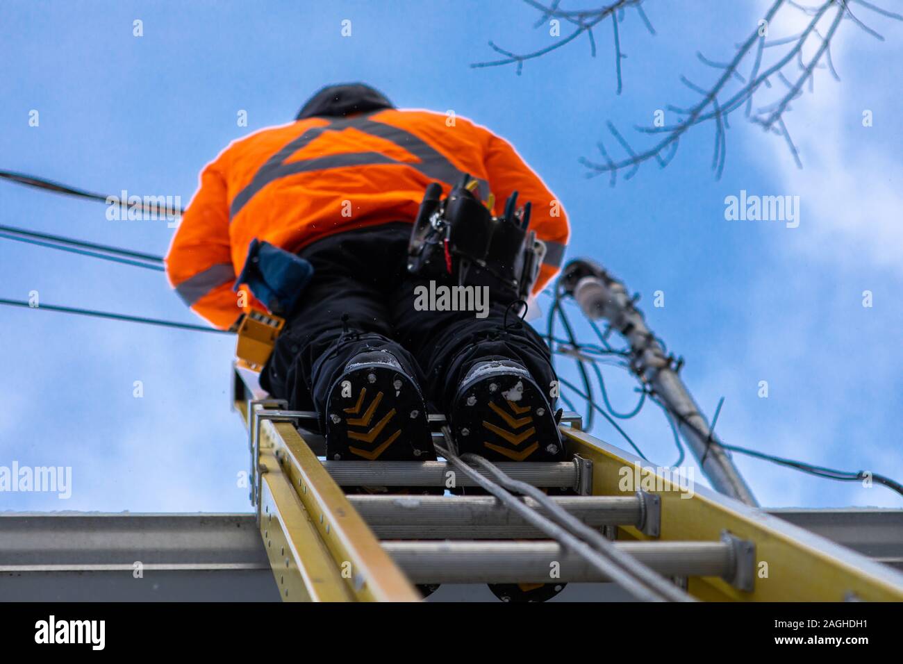 Un professionista telecoms installer è visto da sotto, l'installazione di cavi in fibra ottica dalla cima di una scala sul tetto di una abitazione di proprietà Foto Stock