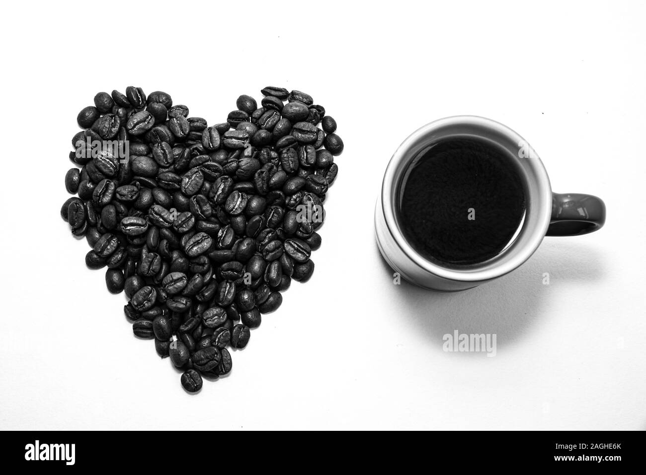 Forma di cuore creato con i chicchi di caffè e una tazza da caffè riempiti con i chicchi di caffè su uno sfondo bianco Foto Stock