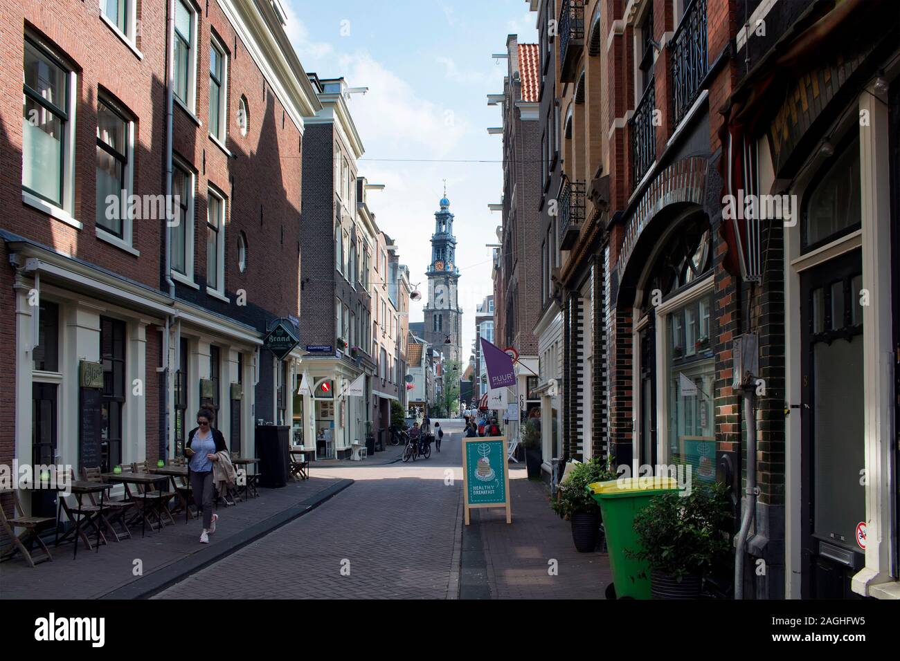 Vista della donna che cammina sulla strada nel quartiere Jordaan, caffetterie e negozi, Westerkerk chiesa la torre in Amsterdam. È una soleggiata giornata estiva. Foto Stock