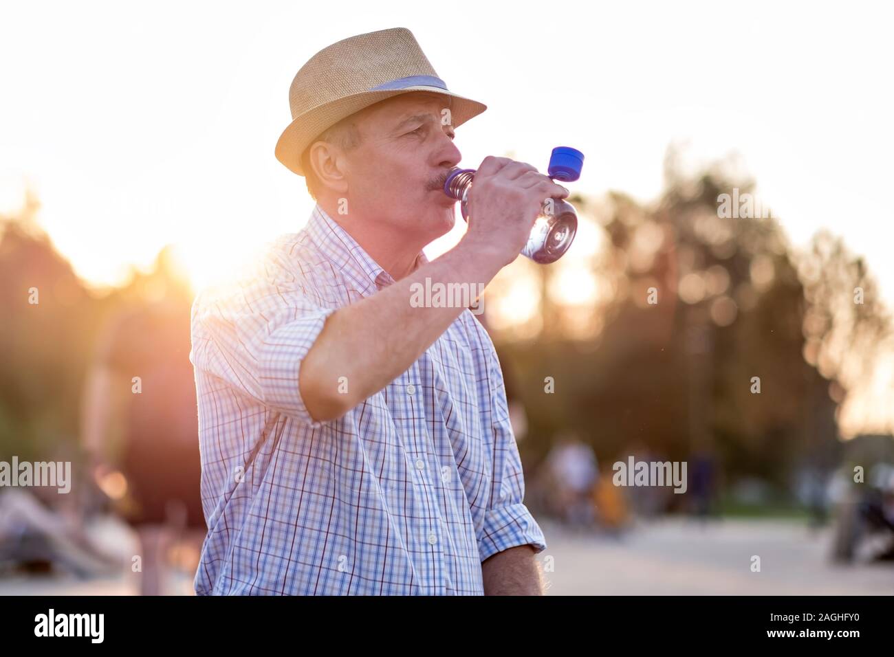 Uomo senior di bere acqua in bottiglia in piedi per esterno Foto Stock