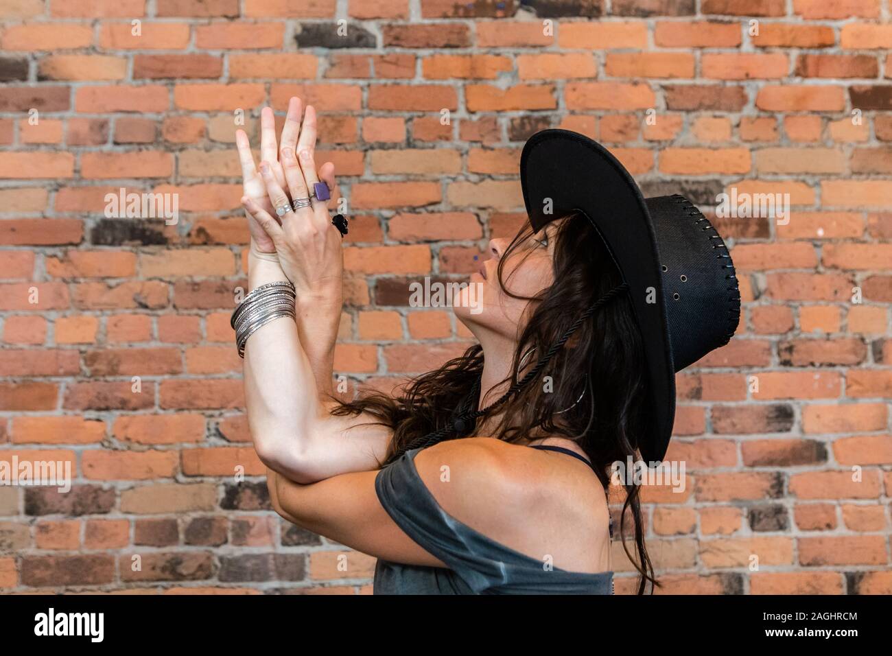 Un profilo laterale posa di una donna che indossa un nero bordata hat come essa si erge in posizione dell'Aquila, Garudasana, un attento bilanciamento yoga permanente la postura Foto Stock