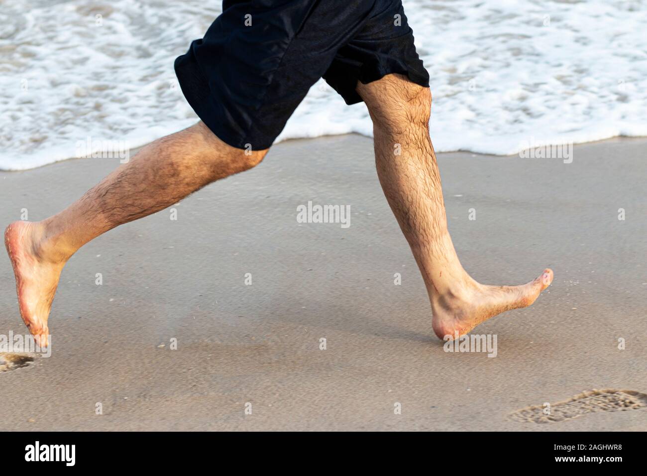 Vista laterale di un runner gambe con nessuna delle scarpe in esecuzione sulla sabbia di una spiaggia vicino all'oceano su Fire Island. Foto Stock