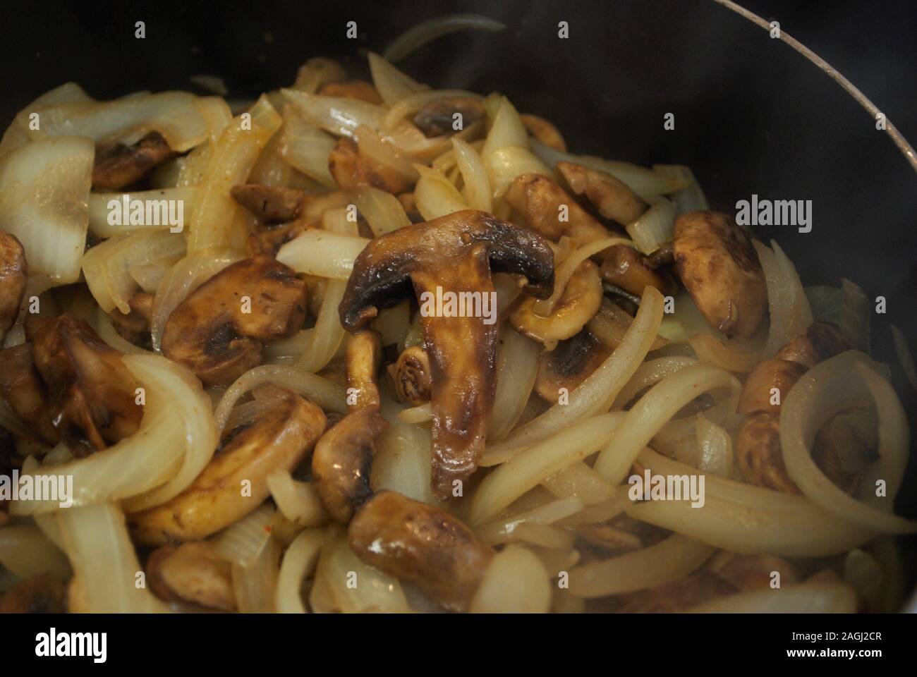 Sauteing i funghi e le cipolle in una padella con olio, condimento, e vapore Foto Stock