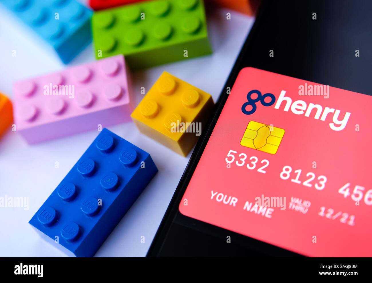 Scheda GoHenry sullo schermo dello smartphone e mattoncini lego accanto ad essa. Scheda con i numeri di dummy. Nessuna delle informazioni sensibili. Messa a fuoco selettiva. Foto Stock