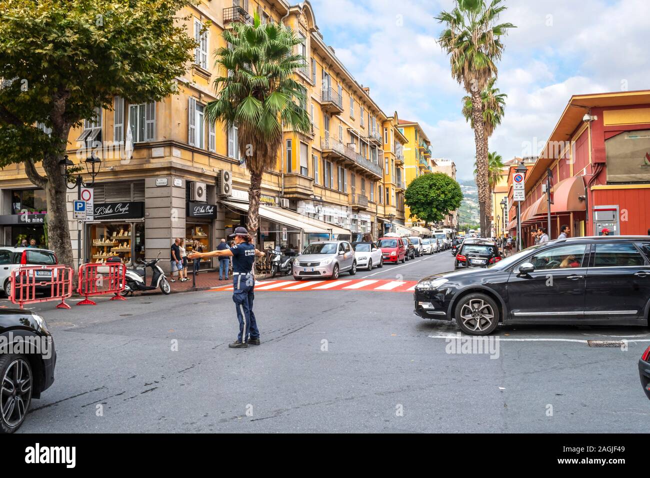 Una femmina la poliziotta dirige il traffico a un rosso e bianco crosswalk nel centro urbano di Ventimiglia, sulla Riviera Italiana. Foto Stock