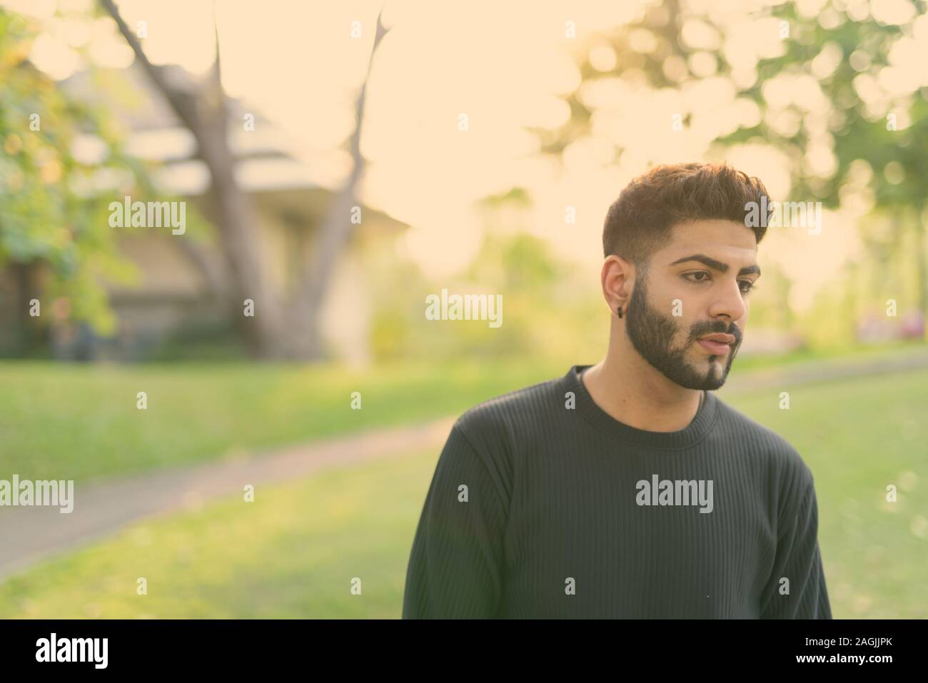 Bel giovane uomo indiano pensare mentre guardando verso il basso sul lato della strada presso il parco Foto Stock