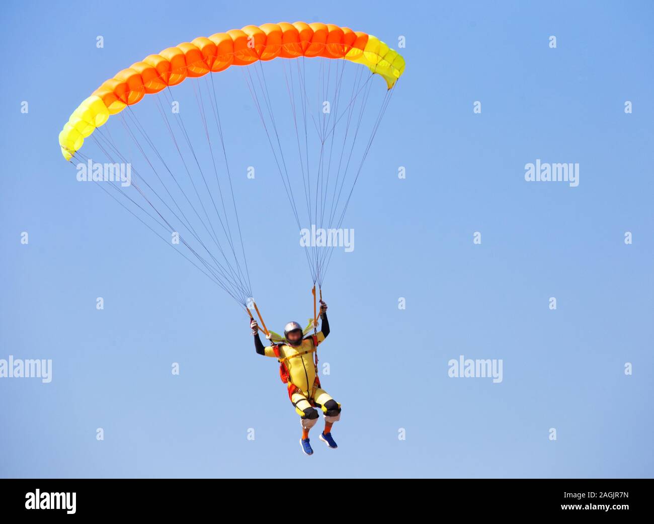 Paracadutista sotto la calotta arancione di un paracadute in un cielo privo di nuvole Foto Stock