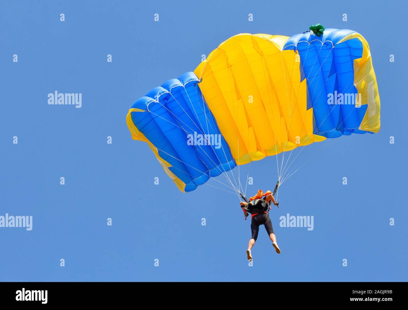 Paracadutista in giallo e blu cupola paracadute nel cielo blu Foto Stock
