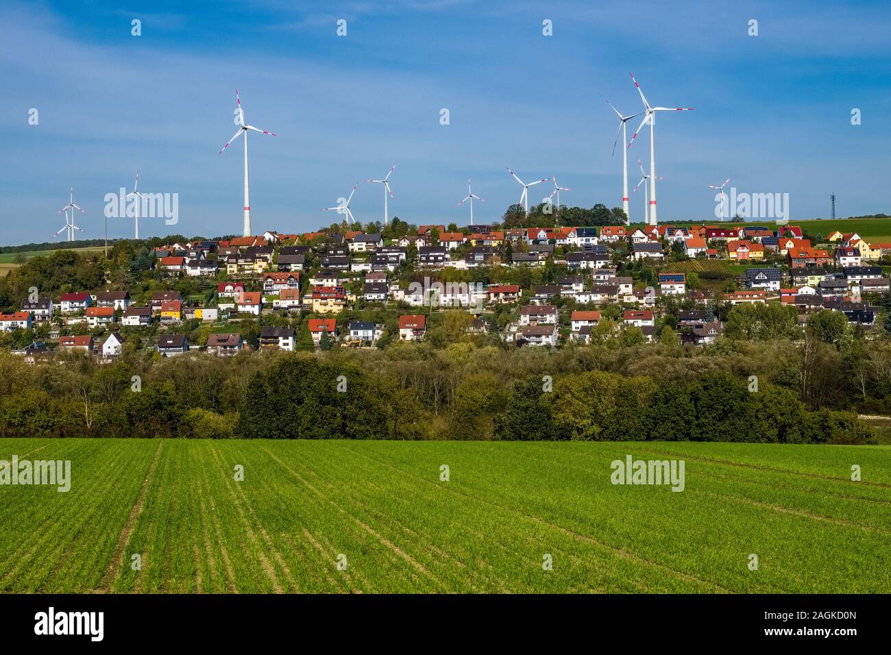 Impianti di energia eolica dietro un agricola utilizzata sul campo e il villaggio, situato tra i campi sul pendio di una collina Foto Stock