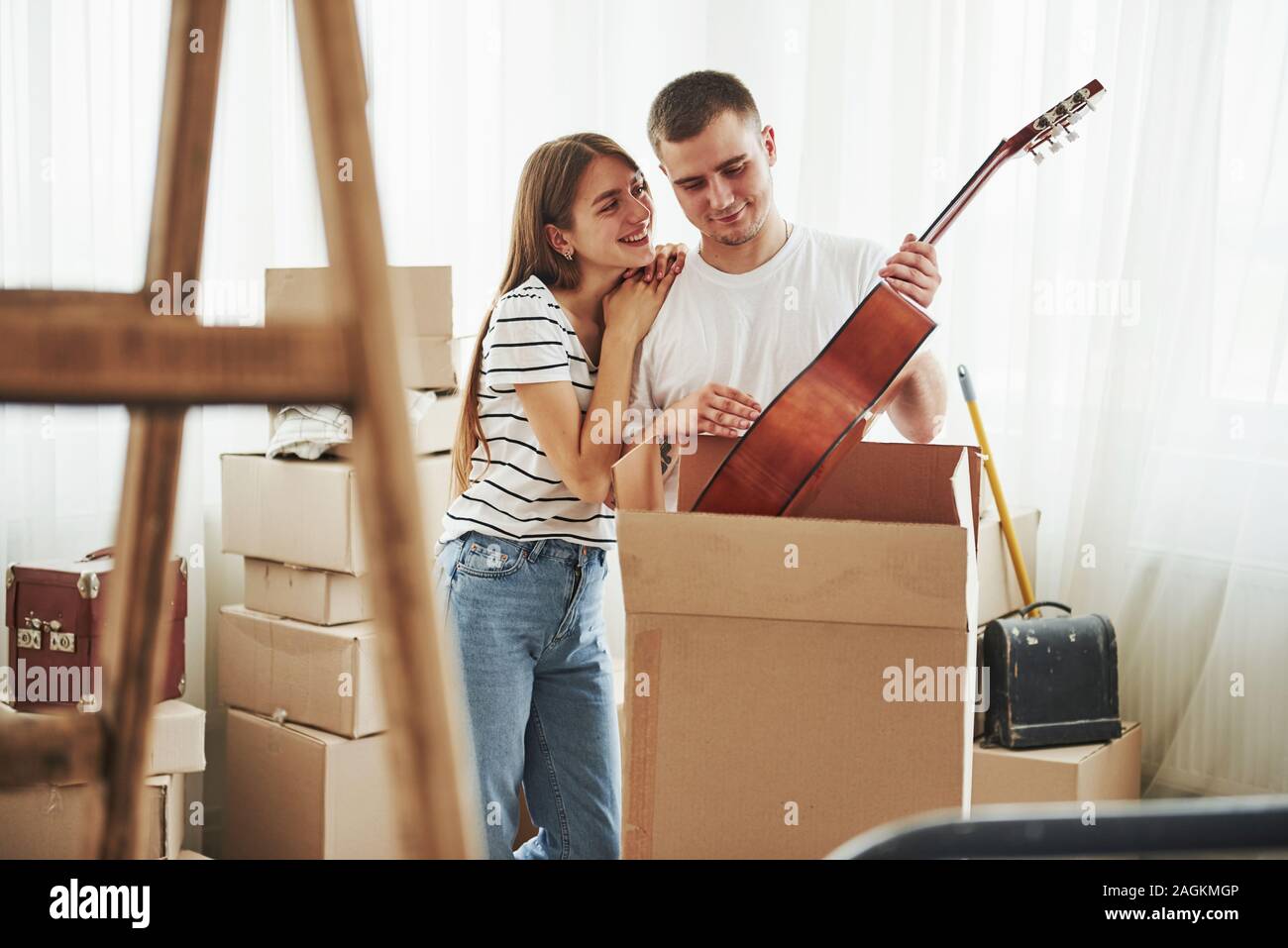 Detiene la chitarra acustica in mani. Allegro coppia giovane nel loro nuovo appartamento. Concezione del movimento Foto Stock