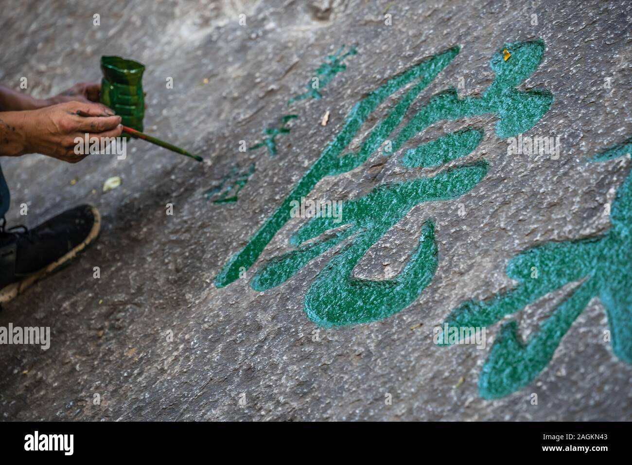 Huashan, Cina - Agosto 2019 : uomo pittura calligrafia cinese caratteri su un grande masso nel cortile di un tempio buddista ai piedi di Hu Foto Stock