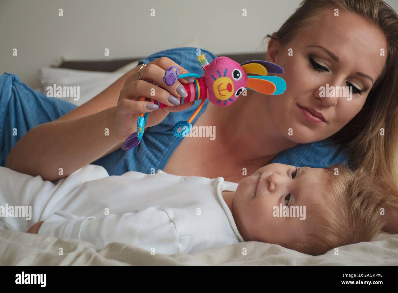 Felice madre con la sua disabili baby boy con paralisi cerebrale sul letto in camera da letto. Giovane biondo mom giocando con suo figlio. Baby guardando il giocattolo. Foto Stock