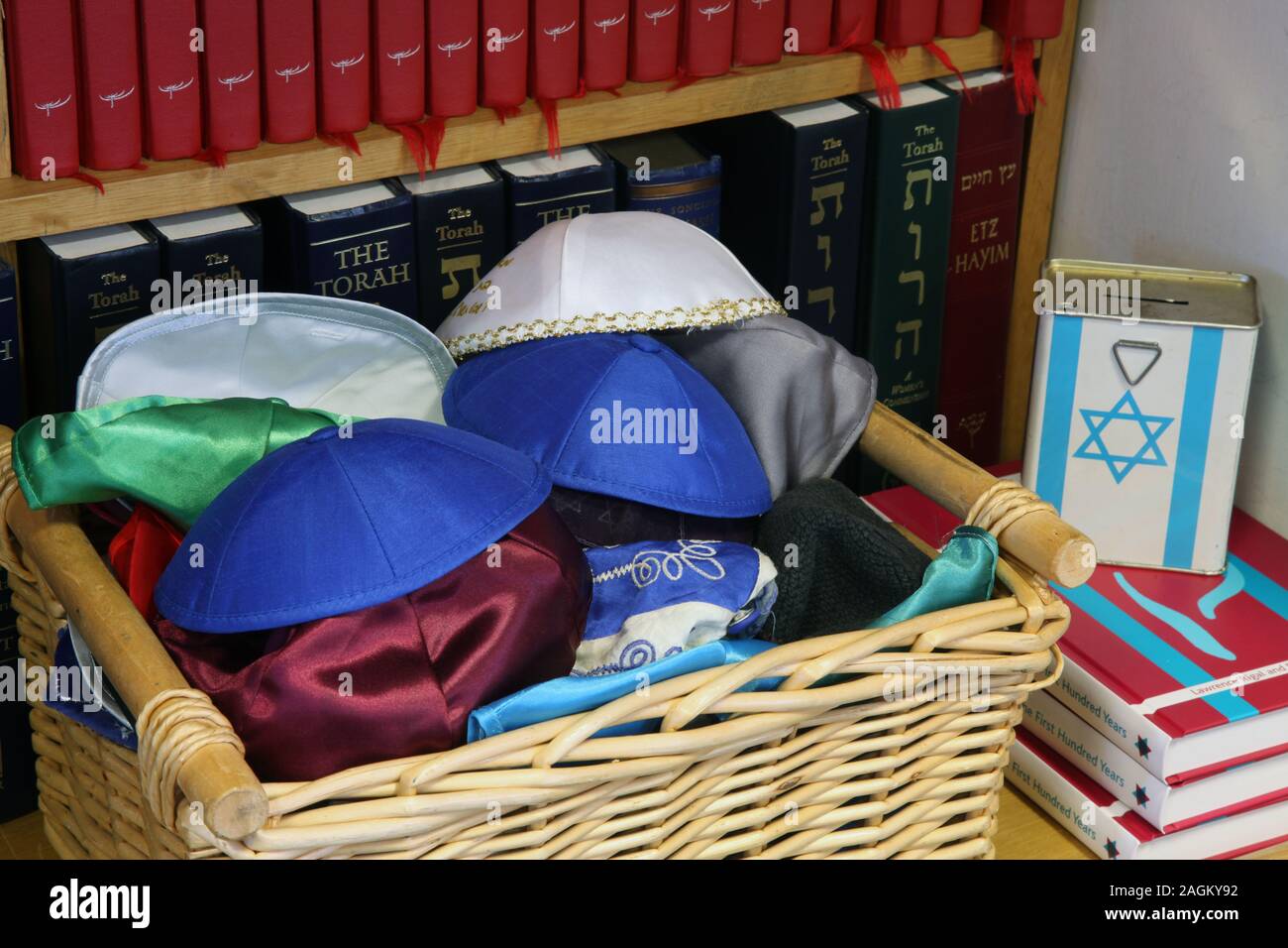 Un cesto di vimini di molteplici Kippa headwear ebraica accanto al Jewish charity box davanti a scaffale Foto Stock