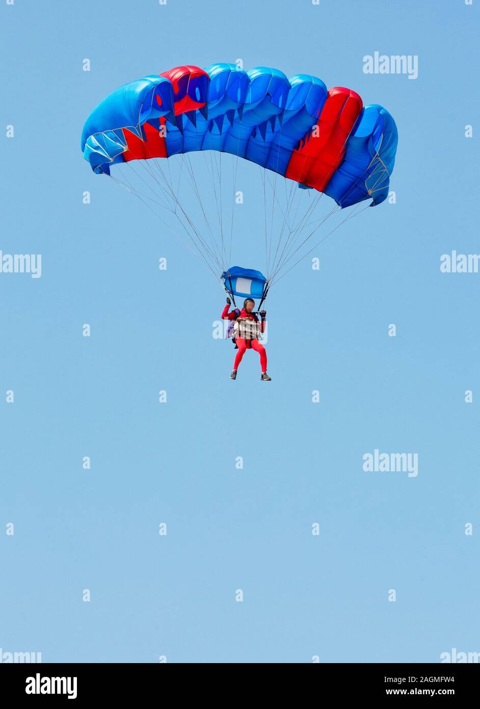 Un paracadutista in tuta rossa scende sotto la tettoia di un paracadute nel cielo blu. Foto Stock