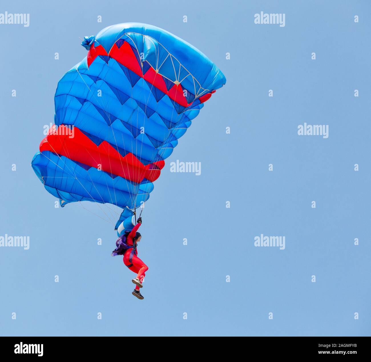 Paracadutista in tuta rossa scende sotto la tettoia del paracadute nel cielo azzurro. Foto Stock