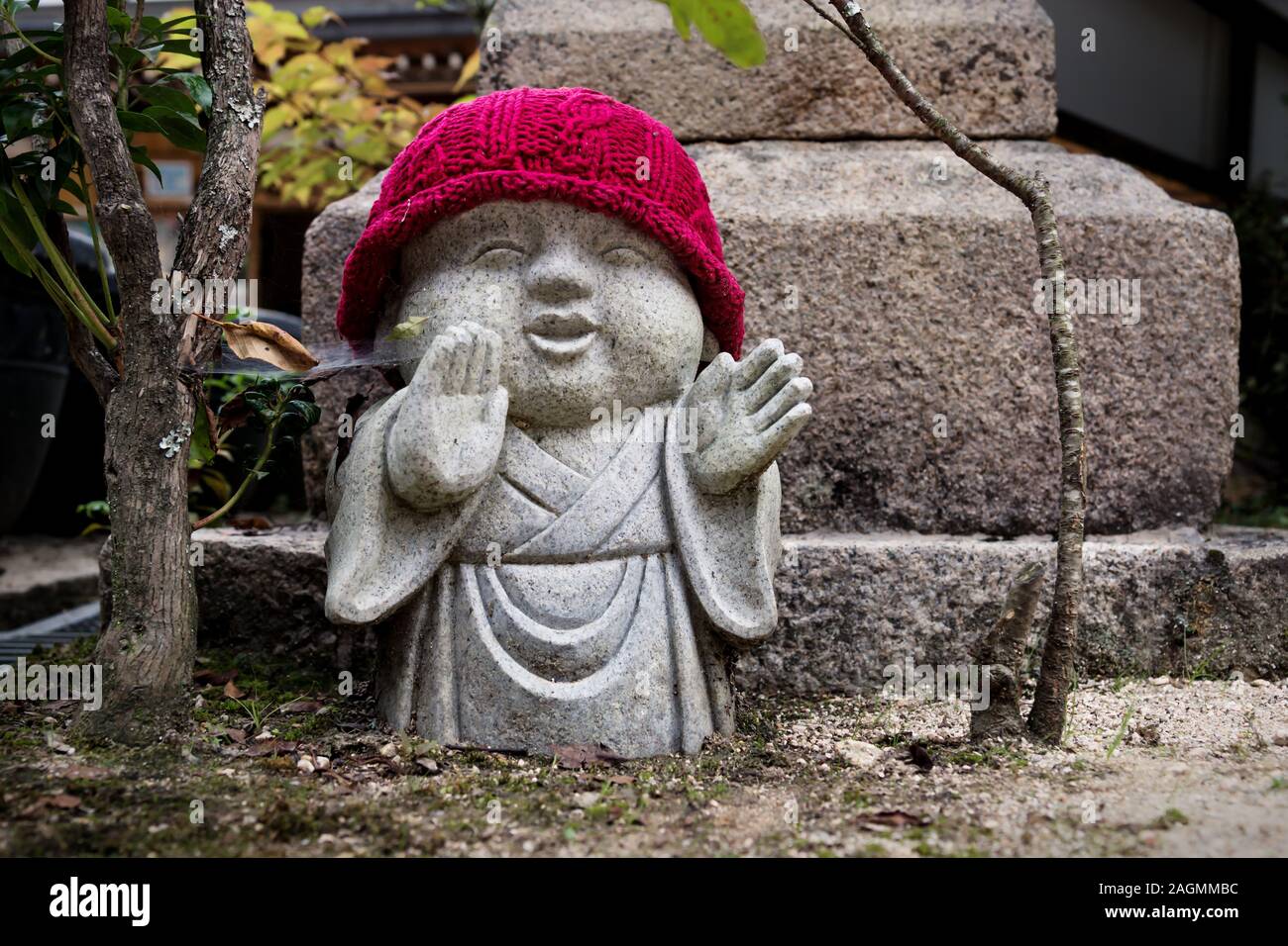 Rakan statua con Red Hat e alberi nel tempio Daishoin nell'isola di Miyajima, Giappone. Foto Stock