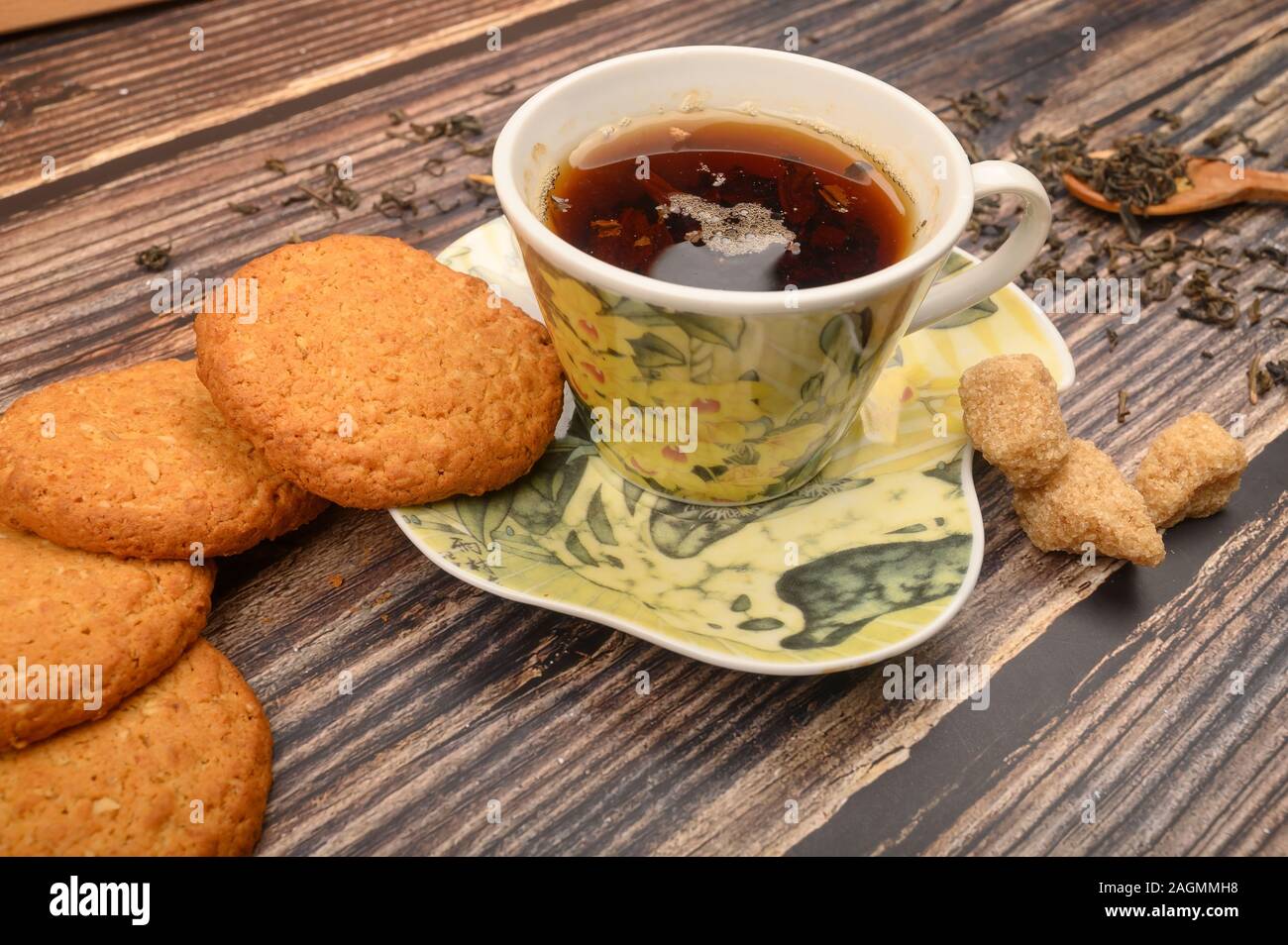 Una tazza di tè nero, foglie di tè, pezzi di zucchero di canna, fiocchi d'avena i cookie su un sfondo di legno. Close up Foto Stock
