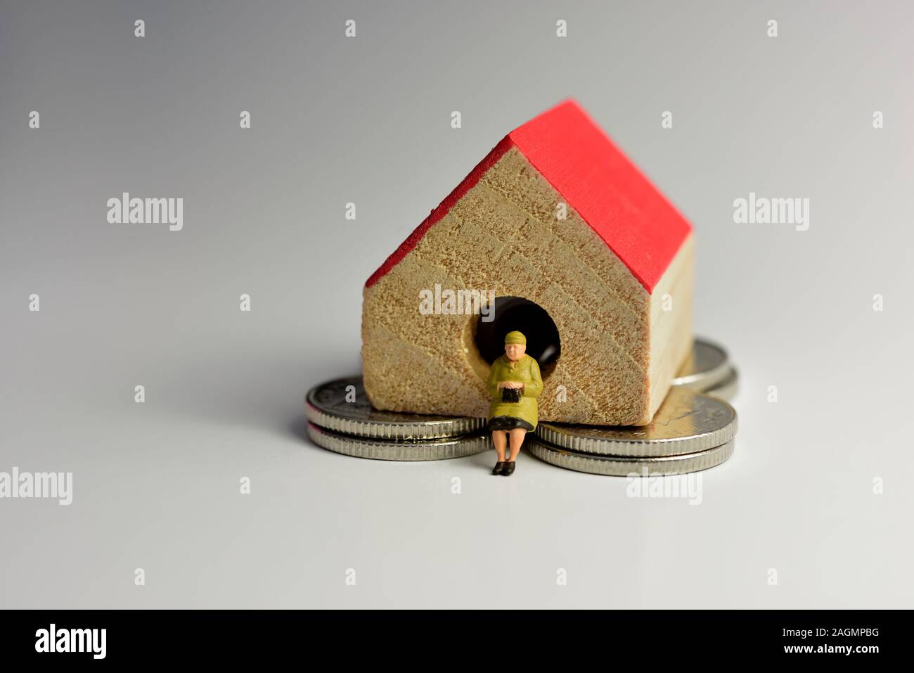Titolare di pensione o di rendita in miniatura, seduto su di una piccola casa con un tetto rosso Foto Stock