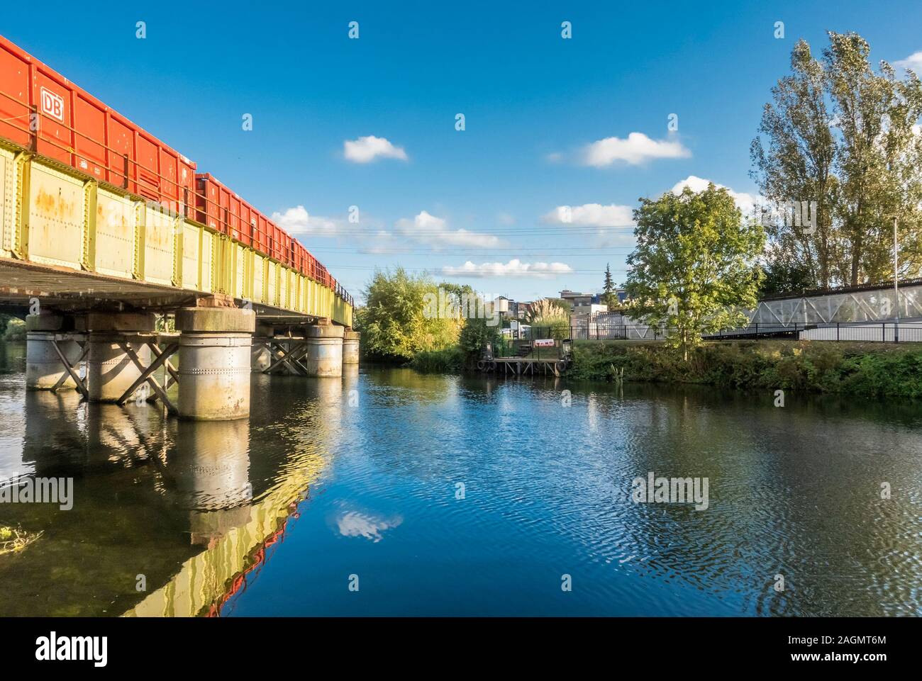 Un arancione treno merci in attraversamento di un verde il ponte ferroviario sul fiume Nene nel centro di Peterborough, Cambridgeshire, Inghilterra Foto Stock