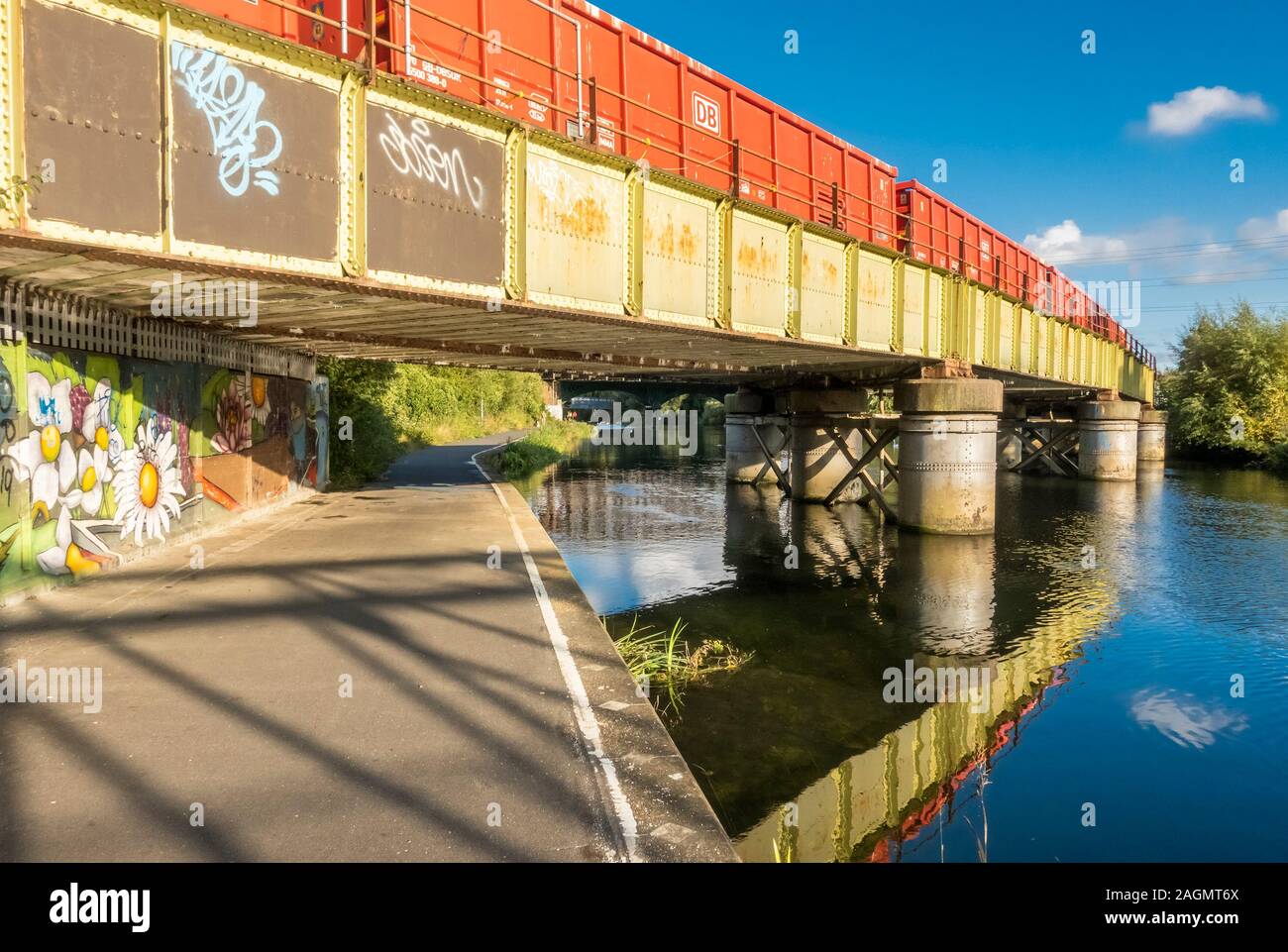Un arancione treno merci in attraversamento di un verde il ponte ferroviario sul fiume Nene nel centro di Peterborough, Cambridgeshire, Inghilterra Foto Stock