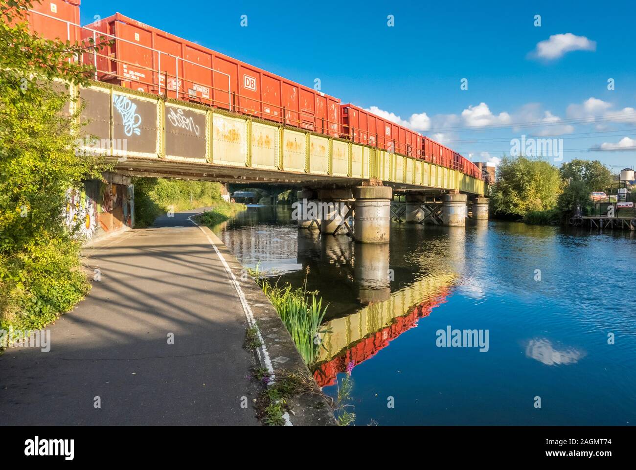 Un arancione treno merci in attraversamento di un verde il ponte ferroviario sul fiume Nene nel centro di Peterborough, Cambridgeshire, Inghilterra Foto Stock