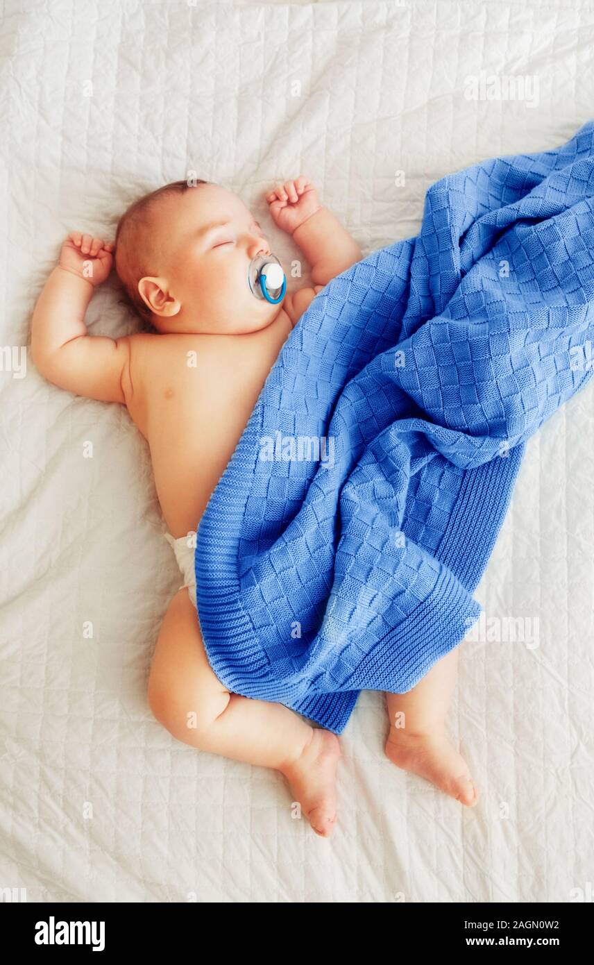 Carino adorabile caucasica neonato bambino dorme sognando il succhietto con il succhietto nella bocca. Neonato sdraiato sul letto coperto con royal blue coperta. Foto Stock