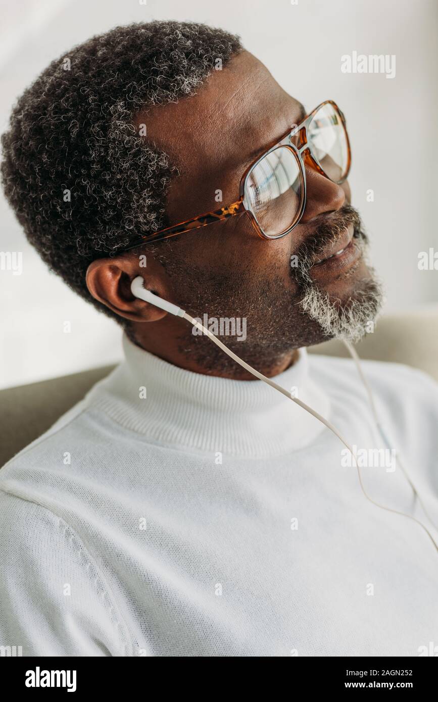 Trasognata African American uomo in bicchieri ascoltando musica in cuffia Foto Stock