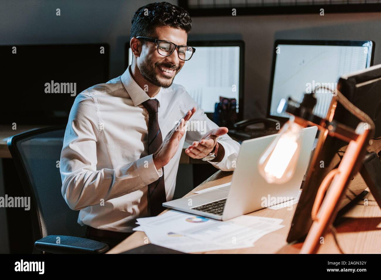 Sorridente e bello bi-razziale trader battendo le mani e guardando il computer portatile Foto Stock