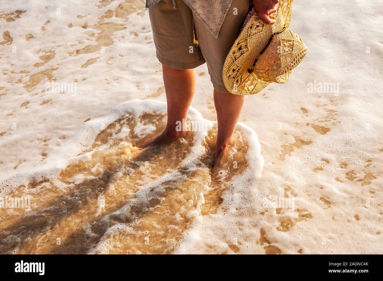 Donna in piedi sulla spiaggia a piedi nudi con onde intorno ai suoi piedi Foto Stock