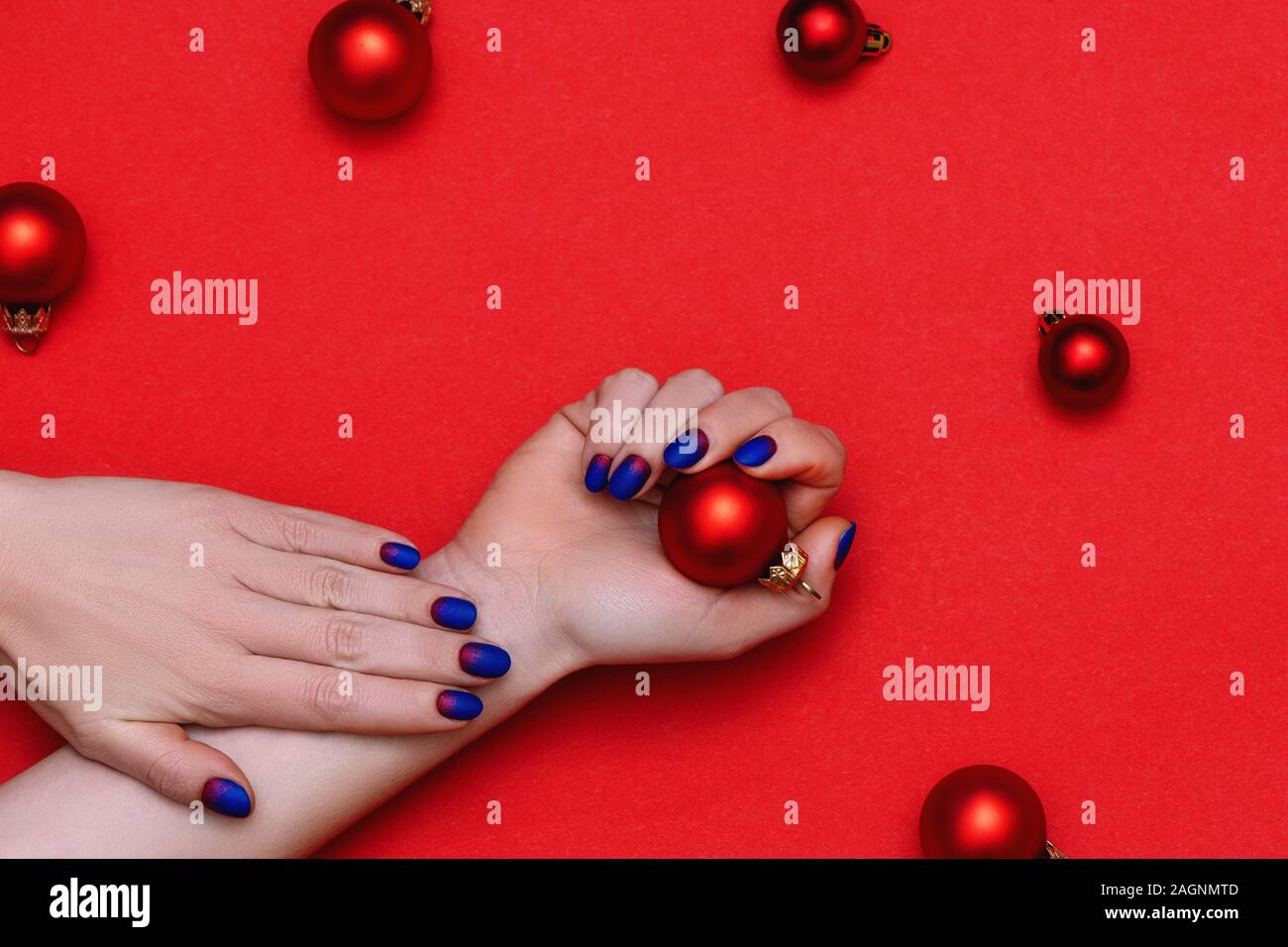 Donna mani con perfetta manicure alla moda azienda giocattolo di Natale su sfondo rosso. Foto Stock