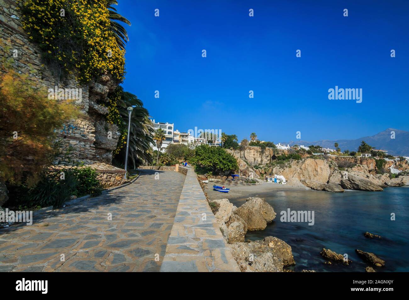 Linea costiera con il sentiero sul mare mediterraneo della spagnola Costa del Sol. La piccola spiaggia di Nerja con rocce e acqua blu sulla giornata soleggiata con blue s Foto Stock