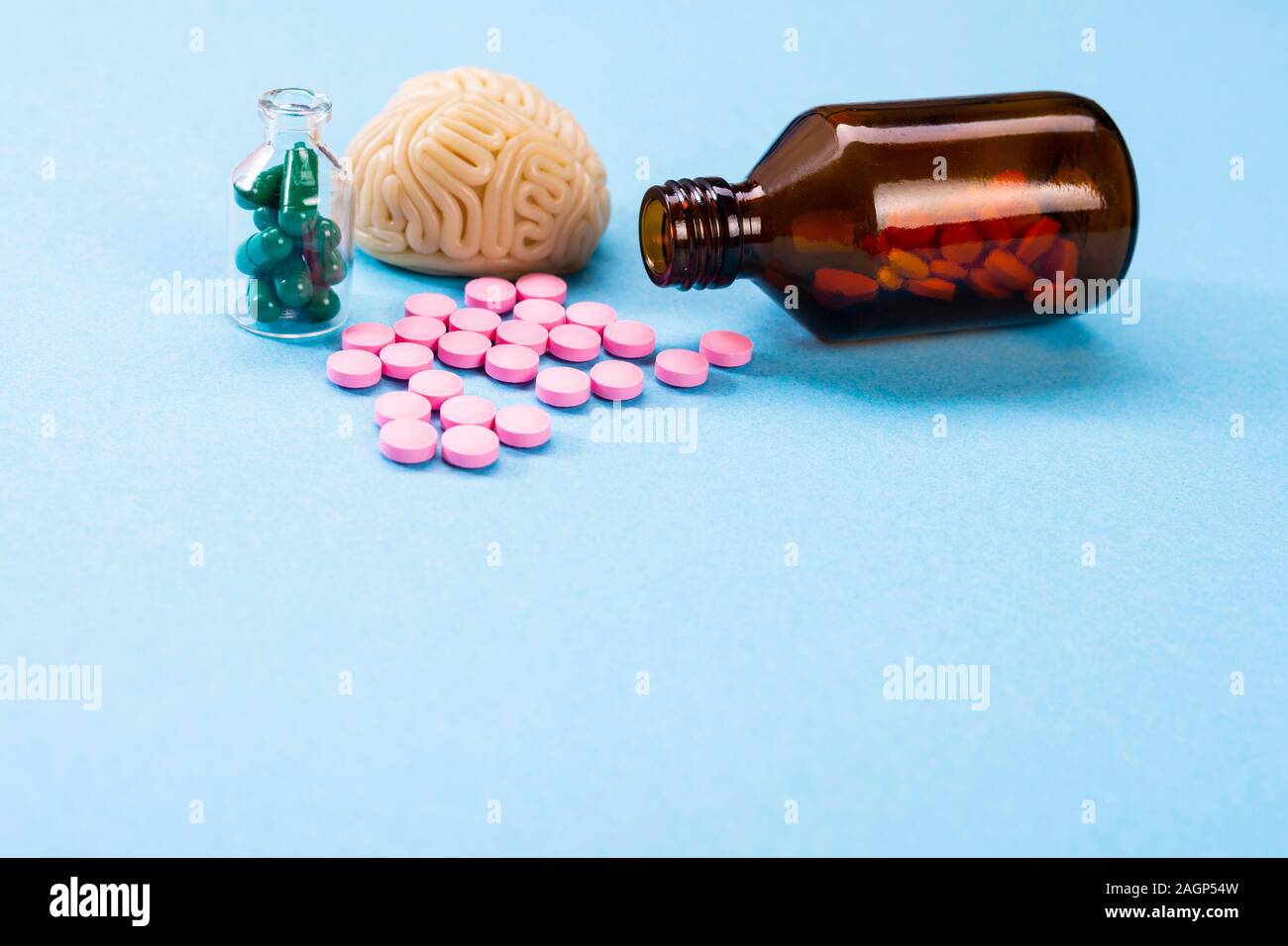 Cervello su uno sfondo blu con rosa e verde pillole in una bottiglia di vetro. Alcune pillole per il cervello. Simbolico per i medicinali, psychopharmaceuticals Foto Stock
