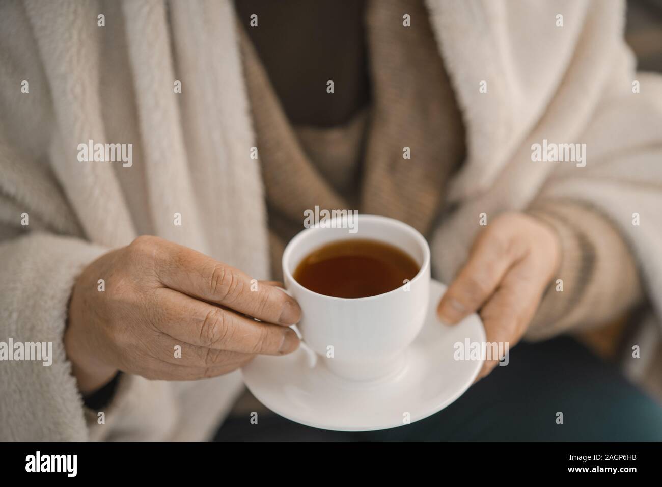 Donna che indossa Cardigan grigio e avvolto in un Plaid di lana tenendo un bianco con la tazza di tè. Close-up shot. Foto Stock