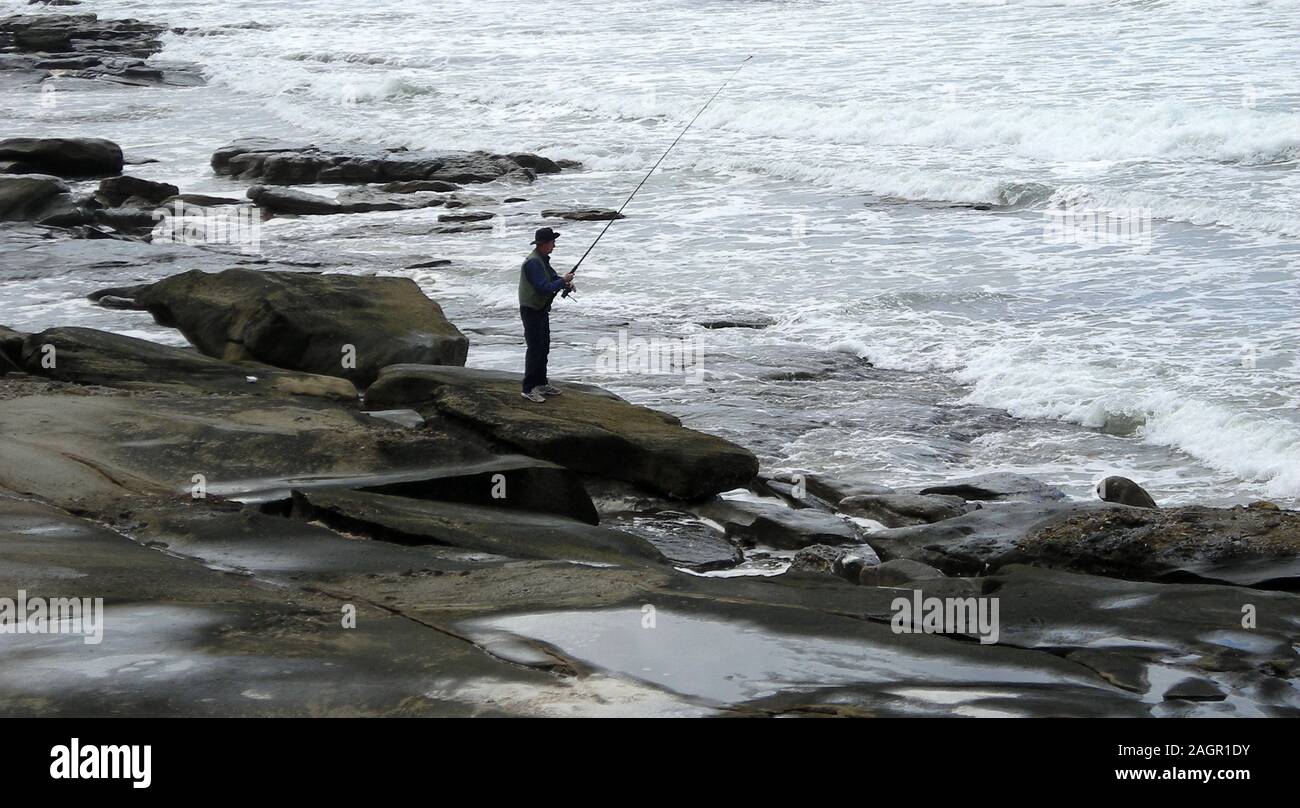 L'uomo la pesca Rocks off a Caloundra, Sunshine Coast, Oceano Pacifico del Sud, Coral Sea, Queensland. Foto Stock