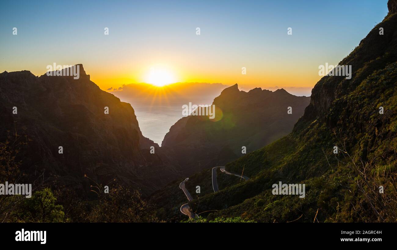 Spagna, Tenerife, arancione tramonto Cielo sopra vista magica oltre masca canyon e strada di montagna tra piante verdi montagne coperte Foto Stock