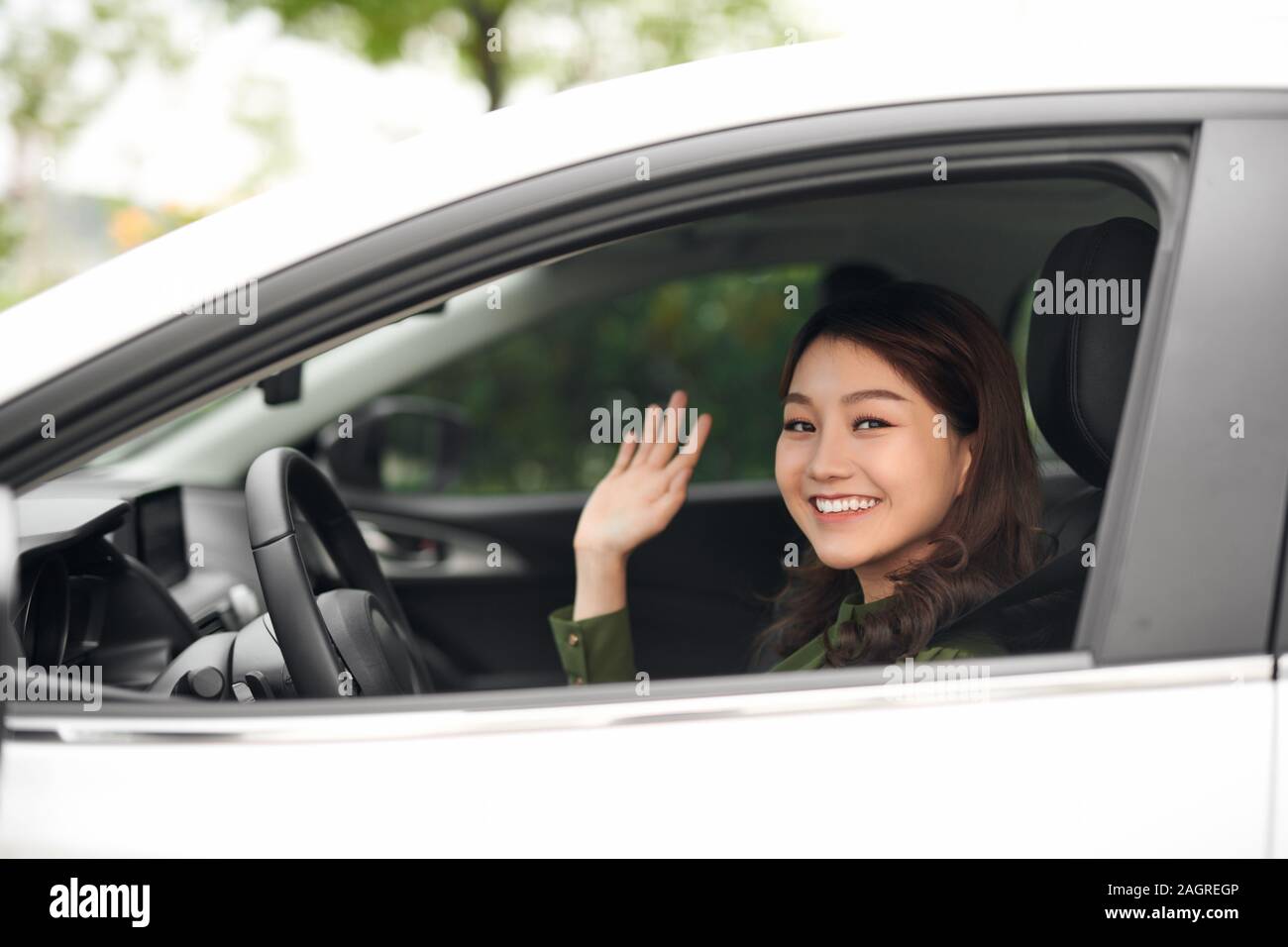 Ciao! Giovane e bella Allegra donna che guarda la fotocamera con il sorriso e sventolare mentre è seduto nella sua auto Foto Stock