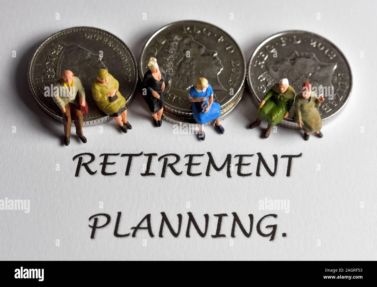 La gente seduta sulle monete dietro la parola pianificazione del pensionamento Foto Stock