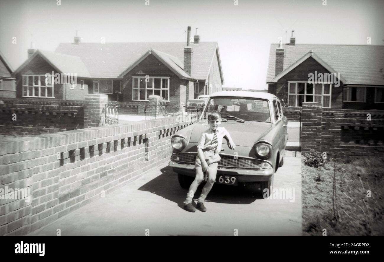 Fotografia o stampa fotografica in bianco e nero di un ragazzo, Terry Waller, di circa 8 anni, appoggiato sul cofano della nuova Ford Anglia di sua madre nel 1960, a St Annes on Sea, Lancashire, Inghilterra, Regno Unito. Foto scattata con una fotocamera Brownie 127, quindi la qualità è limitata. Foto Stock
